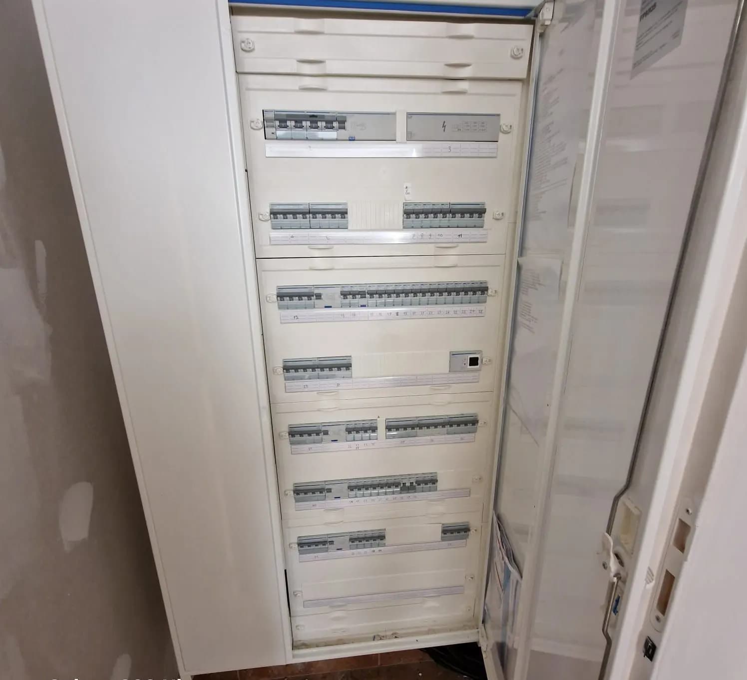 Armoire électrique ouverte avec rangées de disjoncteurs repérés et schémas sur la porte